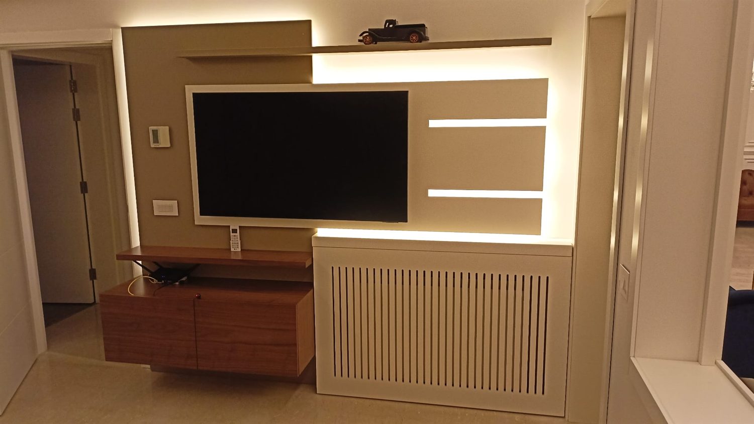 Built-in TV wall with backlit shelving and a slatted radiator cover